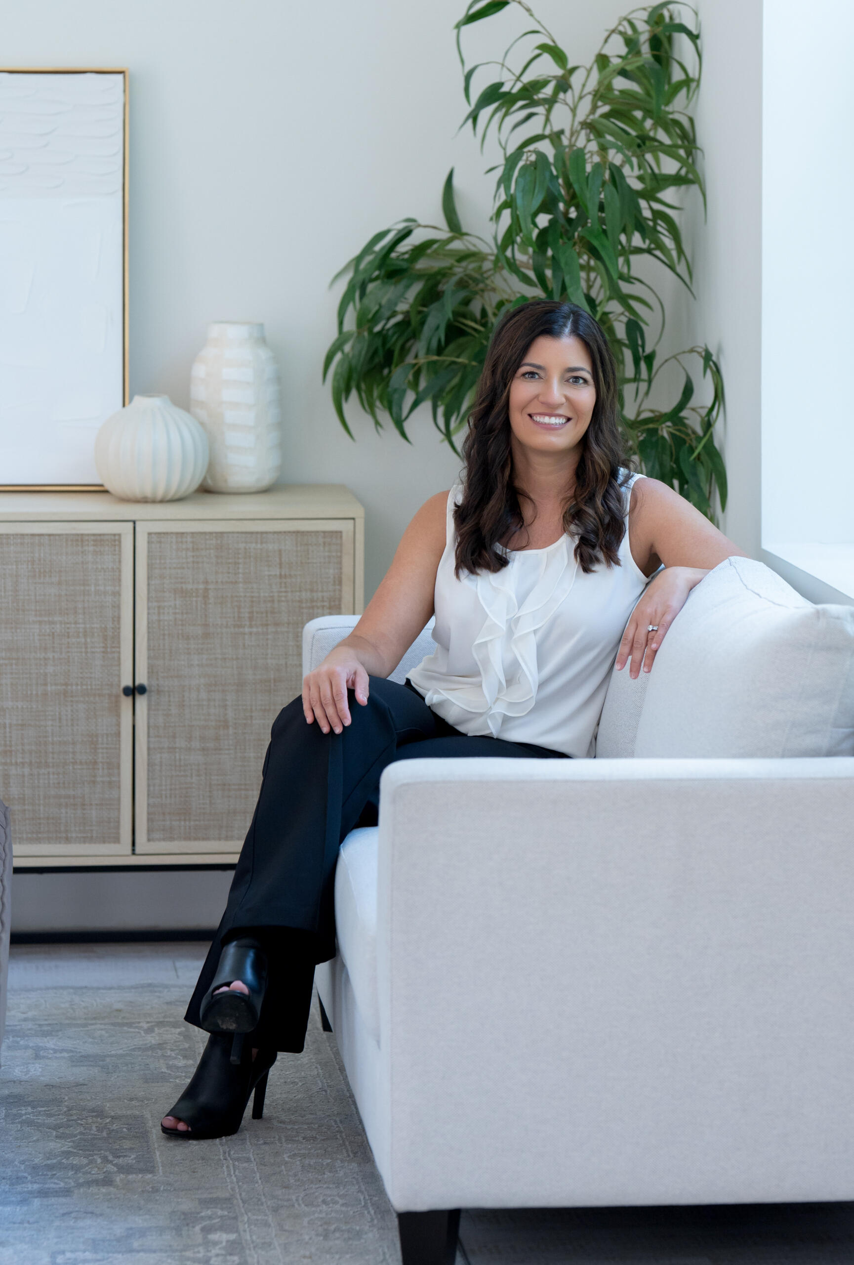 Marika Needham, licensed Realtor serving Massachusetts and Rhode Island, seated on a couch in a bright room, smiling toward the camera